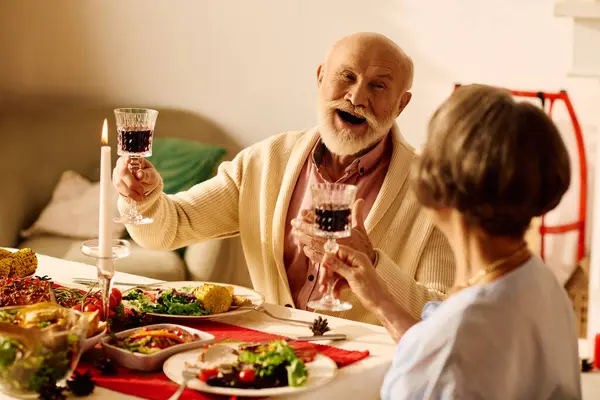 A senior couple raises glasses in joyful celebration during their cozy Christmas dinner at home. — Stock Photo