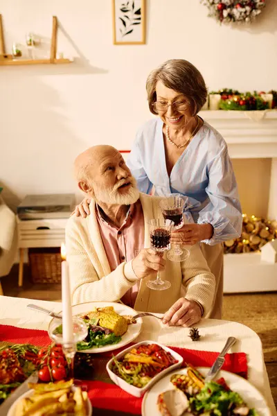 The couple raises their glasses in a toast, surrounded by a festive Christmas feast at home. — Stock Photo