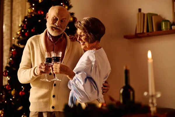 A cheerful elderly couple shares a loving toast at home, surrounded by holiday decorations. — Stock Photo