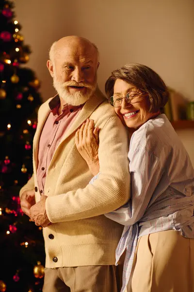 A senior couple shares a warm moment by the Christmas tree, surrounded by joy and love. — Stock Photo