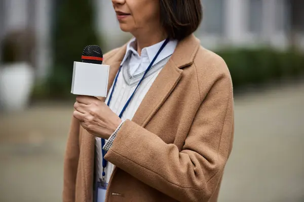 Una donna multirazziale in bilico tiene un microfono, pronta a dare le ultime notizie su una vivace strada della città. — Foto stock