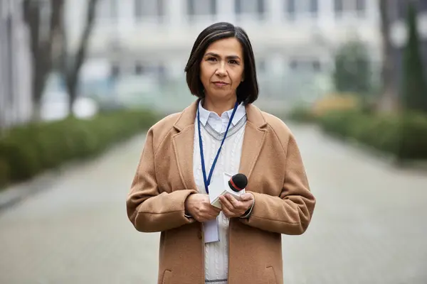 Una giornalista fiduciosa ha un microfono, pronta a dare importanti notizie all'aperto, mostrando la sua professionalità. — Foto stock