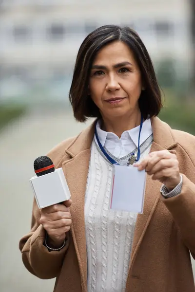 Uma jornalista multirracial segura com confiança um microfone e exibe seu crachá de imprensa — Fotografia de Stock
