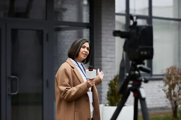 Una giornalista multirazziale femminile tiene un microfono mentre fornisce aggiornamenti di notizie fuori da un edificio contemporaneo. — Foto stock