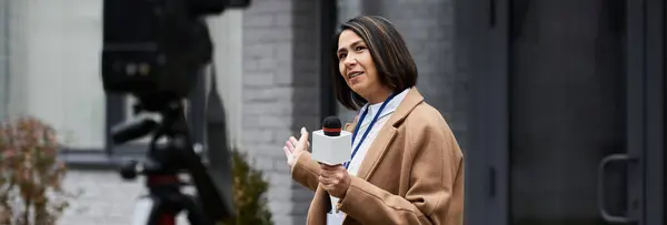 Una giornalista fiduciosa si impegna con il suo pubblico mentre tiene un microfono all'aperto, mostrando la sua professionalità. — Foto stock