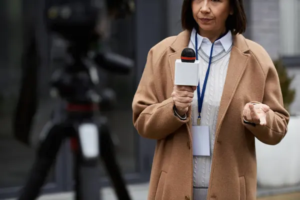 Una periodista multirracial sostiene un micrófono y se prepara para reportar afuera durante la transmisión de noticias. - foto de stock