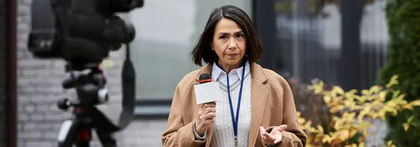 Un giornalista fiducioso detiene un microfono mentre fornisce aggiornamenti all'esterno in un ambiente vivace. — Foto stock