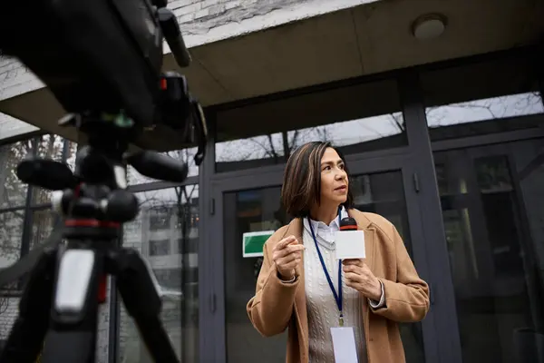 Il giornalista è fiducioso con un microfono, pronto a consegnare le ultime notizie fuori da un edificio moderno. — Foto stock