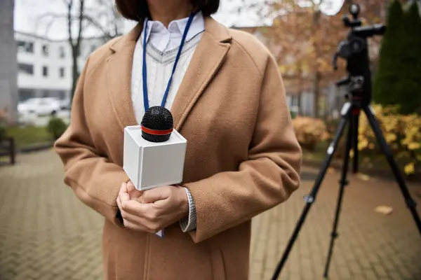 Un giornalista concentrato in possesso di un microfono si trova all'aperto, preparandosi a consegnare un notiziario in mezzo al fogliame autunnale. — Foto stock