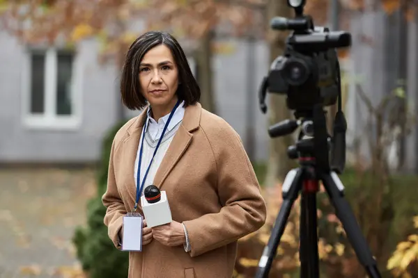 Una giornalista multirazziale femminile tiene con fiducia un microfono, pronto a riferire in autunno. — Foto stock