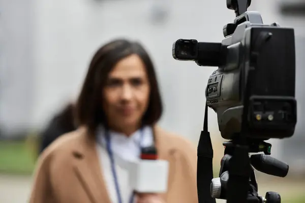 Una giornalista multirazziale indossa un cappotto beige, rivolgendosi con fiducia alla macchina fotografica con un microfono in mano. — Foto stock
