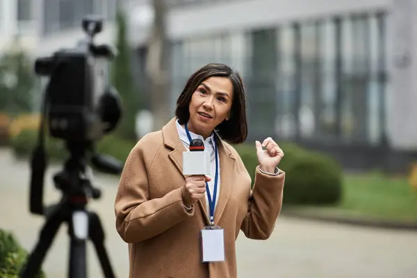 A dedicated journalist passionately shares breaking news while holding a microphone outdoors, engaging viewers. — Stock Photo