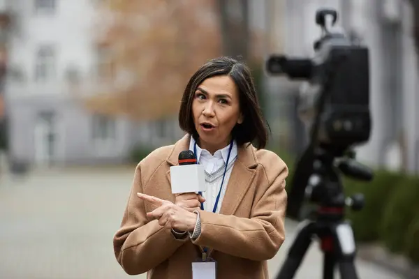 Uma jornalista multirracial compartilha apaixonadamente a notícia enquanto está ao ar livre, microfone na mão. — Fotografia de Stock