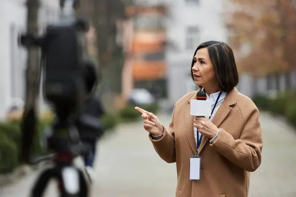 Un giornalista multirazziale tiene un microfono mentre indica e consegna un rapporto di notizie in diretta all'aperto. — Foto stock