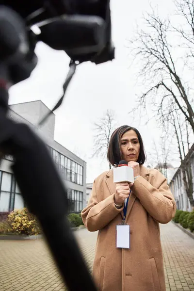 Una giornalista multirazziale ha un microfono, che si prepara a dare notizie all'esterno con un cappotto beige.. — Foto stock