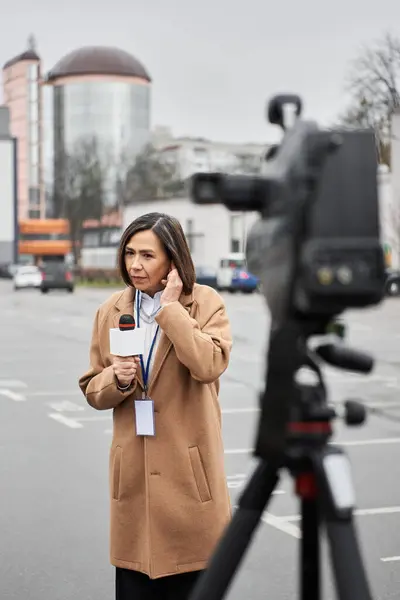 Una giornalista donna prepara il suo microfono per presentarsi in una città affollata, incarnando la resilienza. — Foto stock
