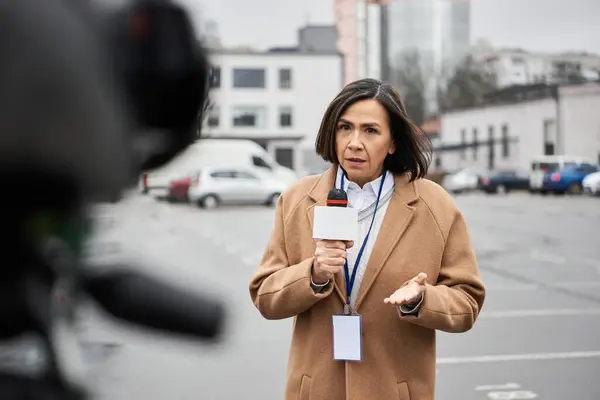 Un giornalista dedicato con un cappotto beige presenta un resoconto in diretta, coinvolgendo il pubblico in un ambiente cittadino. — Foto stock