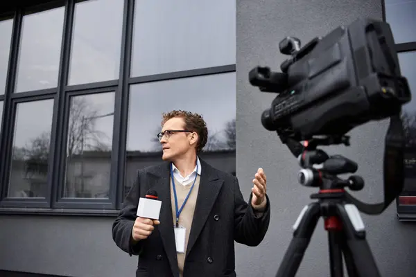 A journalist in glasses and coat actively reports with a microphone in hand, engaging with viewers. — Stock Photo