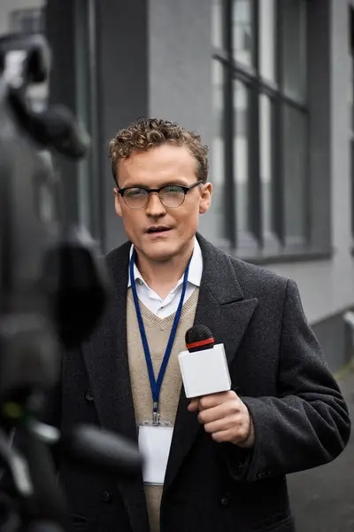 A professional journalist in a coat speaks into a microphone, delivering news updates outdoors. — Stock Photo