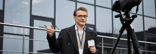 A journalist in glasses passionately reports news outdoors, engaging the audience with a microphone. — Stock Photo