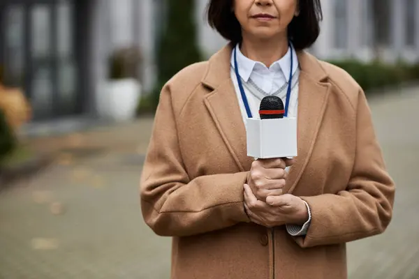 Una giornalista donna ha un microfono, pronta a dare le ultime notizie in un ambiente urbano vivace. — Foto stock