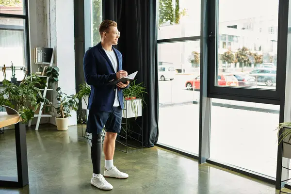 A young businessman with a disability stands confidently, engaging in work at a stylish modern office. — Stock Photo