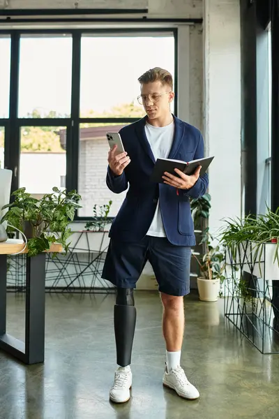 Un joven profesional con una pierna protésica utiliza su teléfono inteligente mientras equilibra las tareas de trabajo en una oficina moderna. - foto de stock