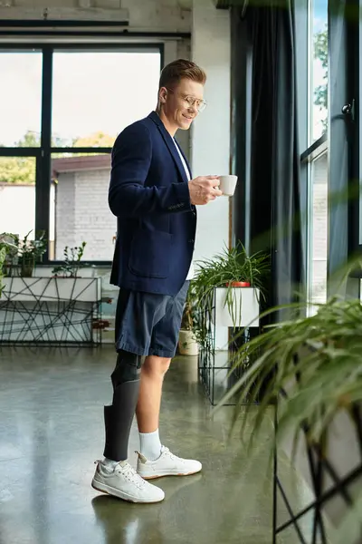 Um jovem empresário bebe café enquanto olha para fora de uma grande janela em um escritório elegante. — Fotografia de Stock