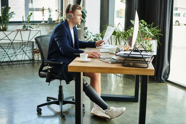 Um jovem com deficiência trabalha diligentemente em sua mesa moderna, mostrando determinação e inclusividade. — Fotografia de Stock