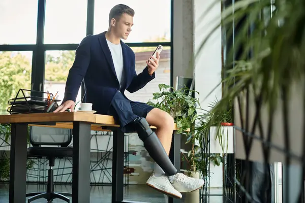 Un joven y ambicioso hombre de negocios con discapacidad se involucra con su teléfono inteligente mientras está en el trabajo. - foto de stock