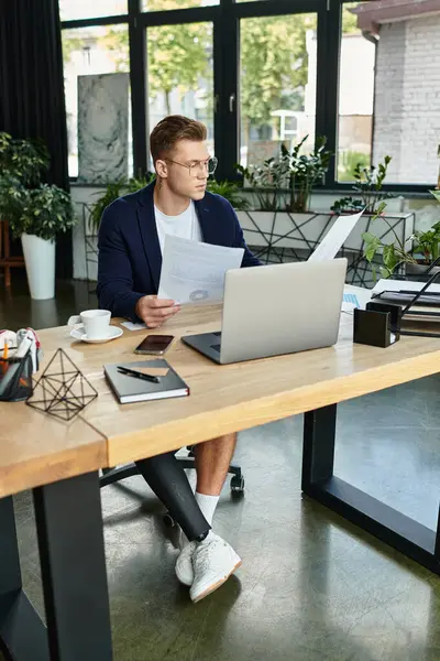 A professional man with an artificial limb reviews documents while seated at a sleek modern desk. — Stock Photo