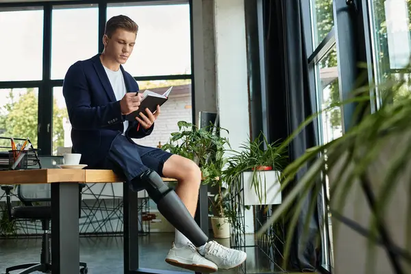 A young and confident man with an artificial limb sits at a desk, writing diligently in a sleek office environment. — Stock Photo