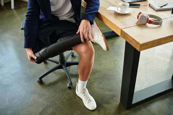 Ein junger Geschäftsmann mit Behinderung passt seine Prothese an, während er in einem modernen Büroarbeitsplatz sitzt. — Stockfoto