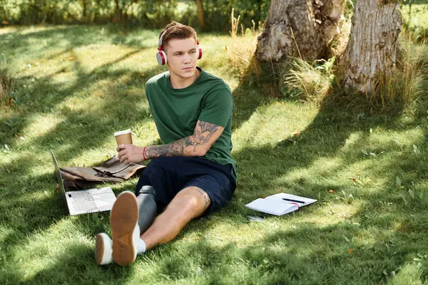 A young man relaxes outdoors with a coffee, headphones on, embracing nature while expressing diversity and inclusion. — Stock Photo