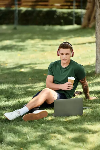 A young man with a disability sips coffee, focused on his laptop in a sunny outdoor setting. — Stock Photo
