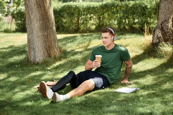 Um homem jovem e bonito senta-se confortavelmente na grama com sua perna protética, tomando café e relaxando. — Fotografia de Stock