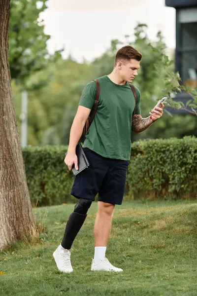 A young man steps confidently through a park, engaging with his phone amid the beauty of nature. — Stock Photo