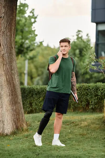 Un hombre joven y guapo con una pierna protésica se para en un parque verde, contemplando su próxima aventura. - foto de stock