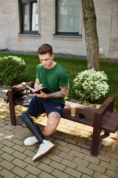 A young man with a prosthetic leg enjoys the outdoors while jotting down thoughts in his notebook. — Stock Photo