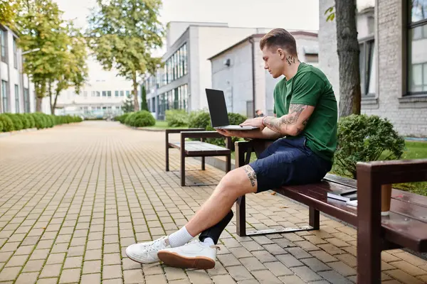 A young man sits on a bench, focusing on his laptop, showcasing determination and inclusion in a serene environment. — Stock Photo