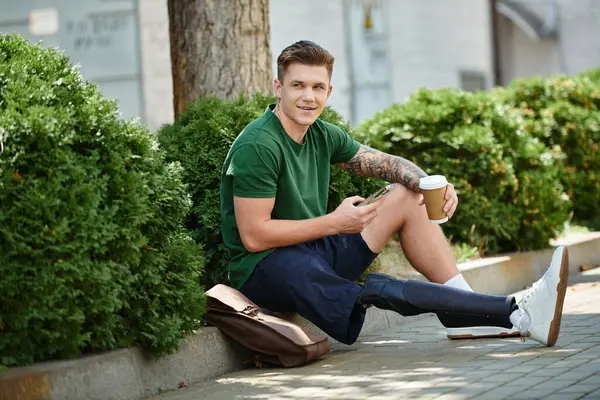 Un joven con una pierna protésica se relaja en un día soleado, disfrutando del café entre una exuberante vegetación. - foto de stock