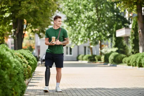 A young man with a prosthetic leg strolls confidently in a bustling park, enjoying his coffee. — Stock Photo