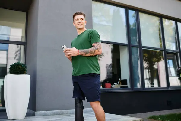 Um homem jovem e elegante fica ao ar livre, confiantemente usando seu smartphone com um sorriso em seu rosto. — Fotografia de Stock
