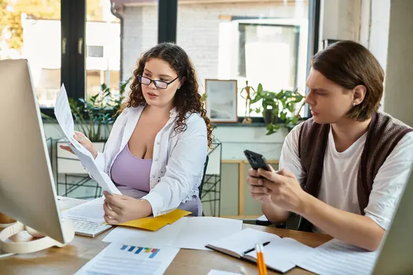 A young plus size woman reviews documents while her male friend casually checks his phone nearby. — Stock Photo