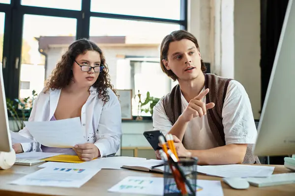 A young plus size woman and her male friend are discussing ideas while working at a desk together. — Stock Photo