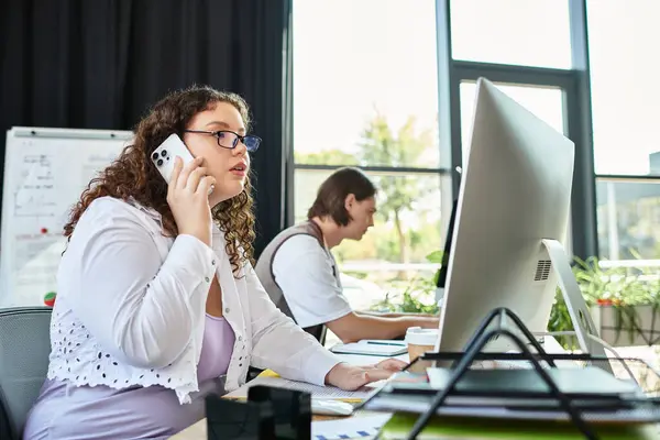 A young plus size woman speaks on her phone, collaborating with her friend in a vibrant workspace. — Stock Photo