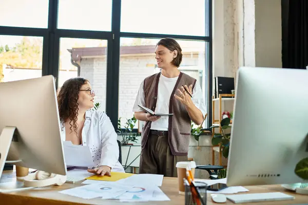 A plus size woman and her male friend engage in lively conversation at their workspace. — Stock Photo