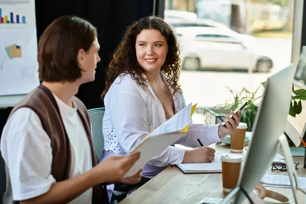 Una joven mujer de talla grande comparte ideas con su amigo varón mientras trabaja en un espacio de trabajo elegante. - foto de stock