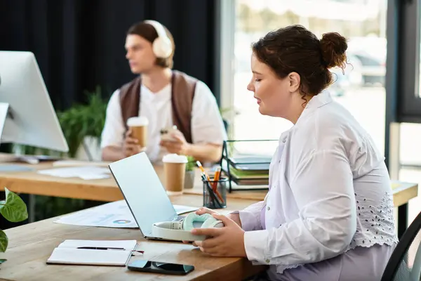 A young plus size woman focuses on her laptop while her friend enjoys a drink beside her. — Stock Photo