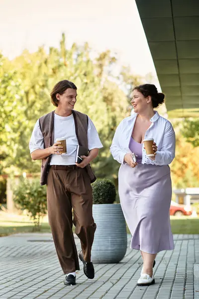 A young woman and her male friend joyfully walk together, sipping coffee amid vibrant greenery. — Stock Photo